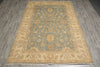 Load image into Gallery viewer, A rectangular area rug with an ornate traditional floral pattern, featuring a muted blue-gray center field and beige/gold borders, laid out on a gray wood-look floor.