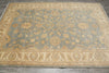 Load image into Gallery viewer, A rectangular area rug with a traditional floral pattern, featuring a muted blue-gray center field and warm beige borders, laid out on a gray floor.