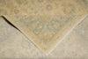 Load image into Gallery viewer, A close-up of an area rug with a faded traditional floral pattern in beige and muted blue-gray tones, showing the corner and fringed edge of the textile.