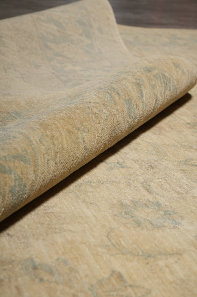 A close-up of a rolled piece of textured fabric or wallpaper in a warm beige tone with subtle muted blue-gray marbled or distressed patterning.