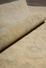 Load image into Gallery viewer, A close-up of a rolled piece of textured fabric or wallpaper in a warm beige tone with subtle muted blue-gray marbled or distressed patterning.