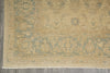 Load image into Gallery viewer, A close-up of a traditional area rug with a faded beige and muted blue-green floral pattern, laid out on a gray tiled floor.