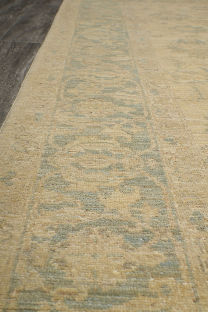 A close-up view of a textured area rug with a distressed traditional pattern in beige and muted blue-gray tones.