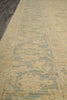 Load image into Gallery viewer, A close-up view of a textured area rug with a distressed traditional pattern in beige and muted blue-gray tones.