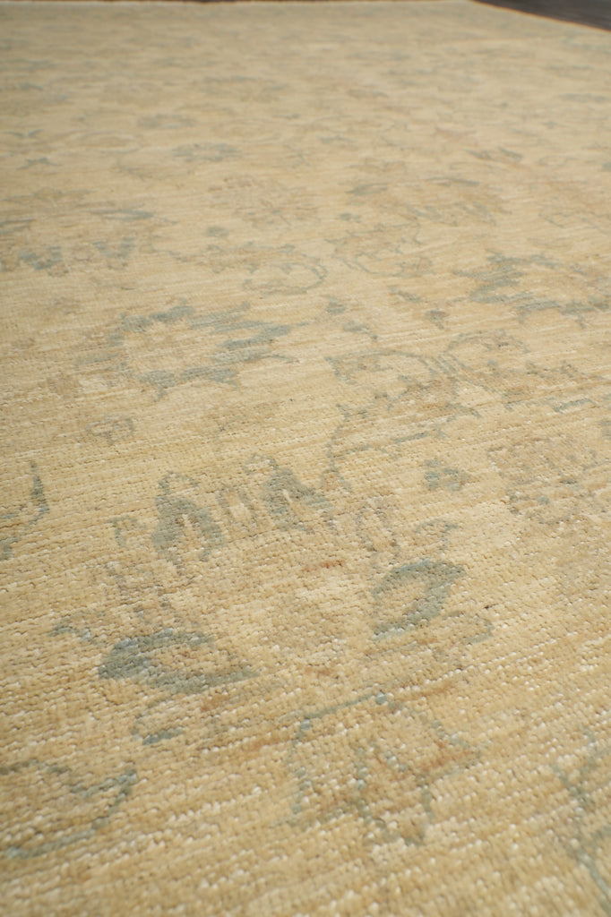 A close-up of a textured rug or fabric in a warm beige tone with faded gray and muted blue-gray distressed patterning.