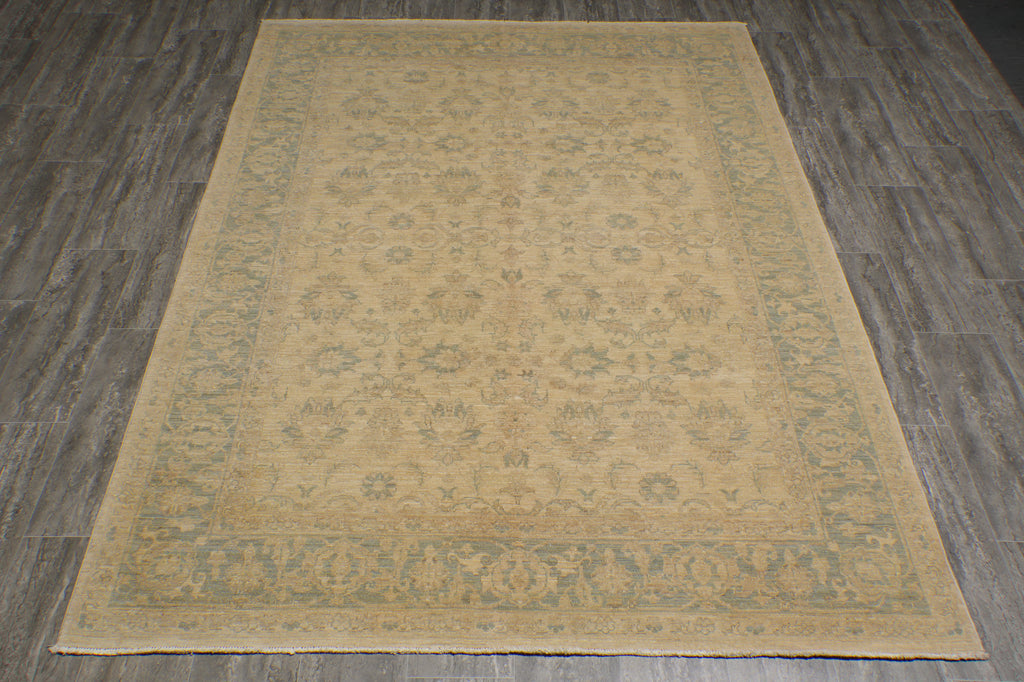 A rectangular area rug with a distressed traditional pattern in beige and muted sage green, laid flat on a dark gray wood-look floor.