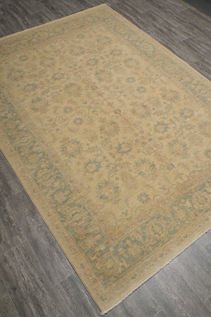A rectangular area rug with a beige and muted blue-gray floral pattern, shown from an overhead angle on a gray wood-look floor.