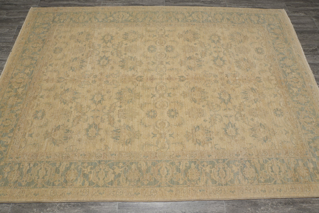 A rectangular area rug with a traditional floral pattern in beige and muted sage green, laid out on a dark gray tiled floor.