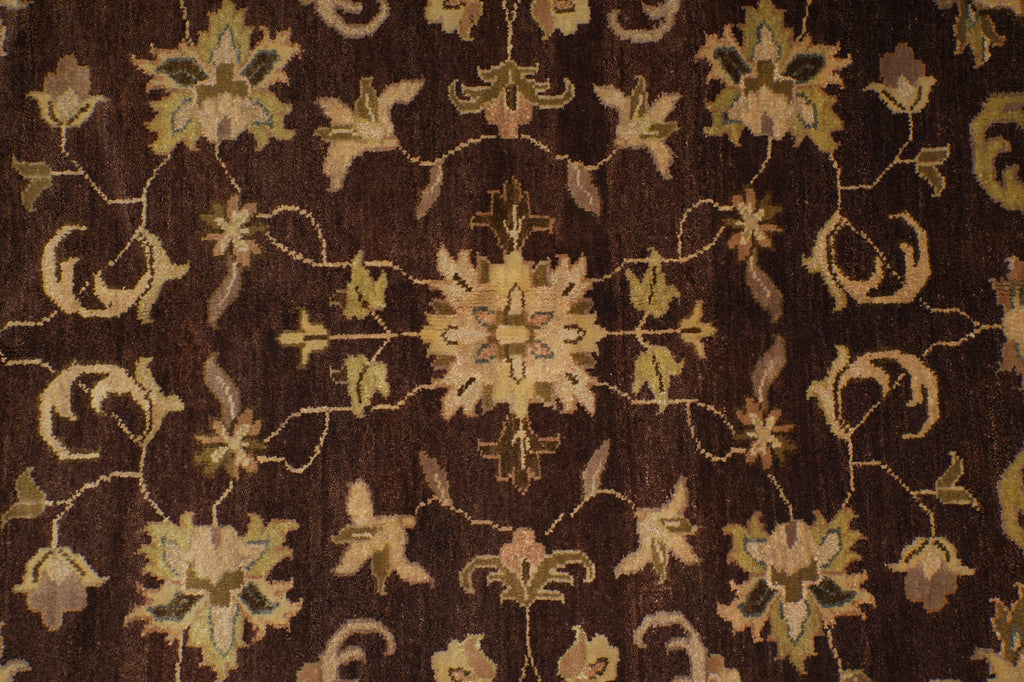 A close-up of a traditional patterned rug with a dark brown background and beige, tan, and muted green floral motifs.