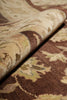 Load image into Gallery viewer, A close-up of a patterned rug or textile with a rolled section showing its texture and design. The color palette features warm brown, beige, cream, and muted olive-green tones in an ornate floral or damask-style motif.