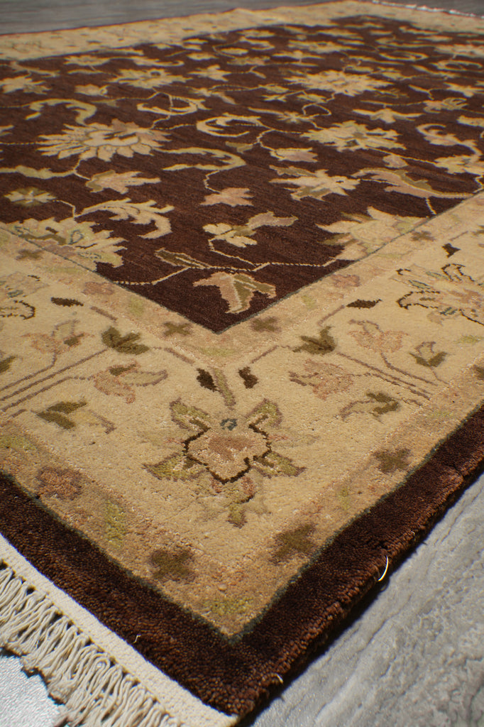 A close-up of a traditional patterned rug showing a cream and beige field with floral motifs, a dark brown border, and a large dark brown panel with cream floral and scroll patterns.