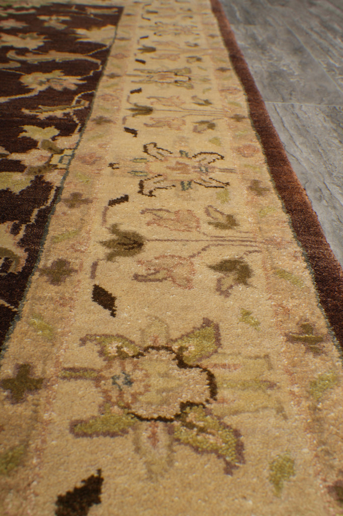 Close-up of a patterned area rug showing a beige central band with floral motifs and a dark brown border, photographed indoors on a gray floor.
