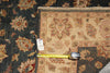 Load image into Gallery viewer, A close-up of a patterned area rug corner with a tape measure placed along the edge to show dimensions. The rug has a beige central field with floral motifs and a dark navy outer section with red and beige detailing.