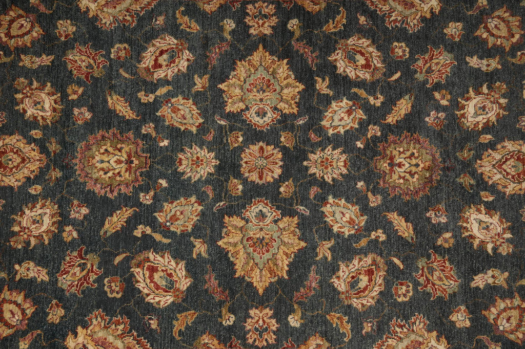 A close-up of a traditional patterned rug or textile with a dark charcoal gray background and ornate floral medallions in beige, rust red, and muted green.