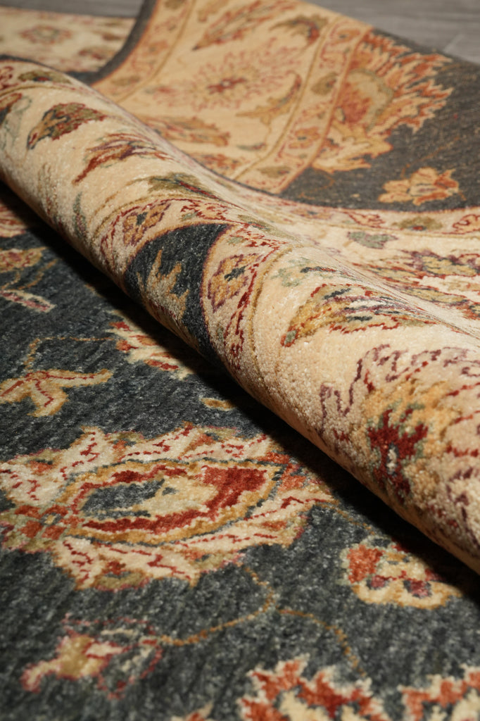 A close-up of a rolled area rug showing its detailed traditional pattern in beige, red, and dark gray.