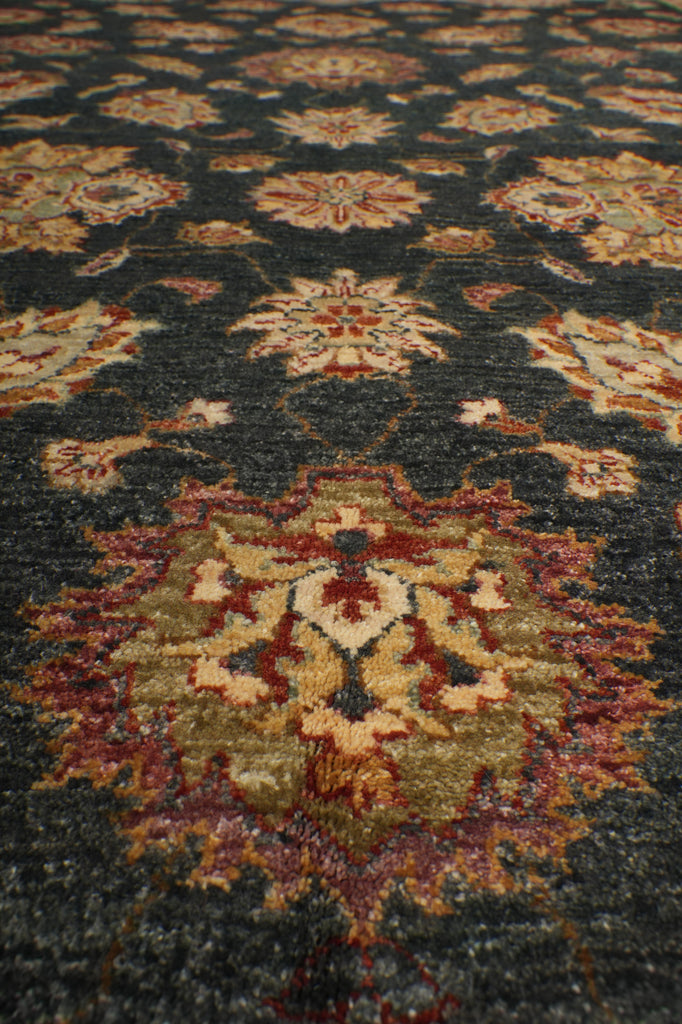A close-up view of a traditional patterned area rug with a dark charcoal gray background and ornate floral motifs in beige, rust red, and muted gold.