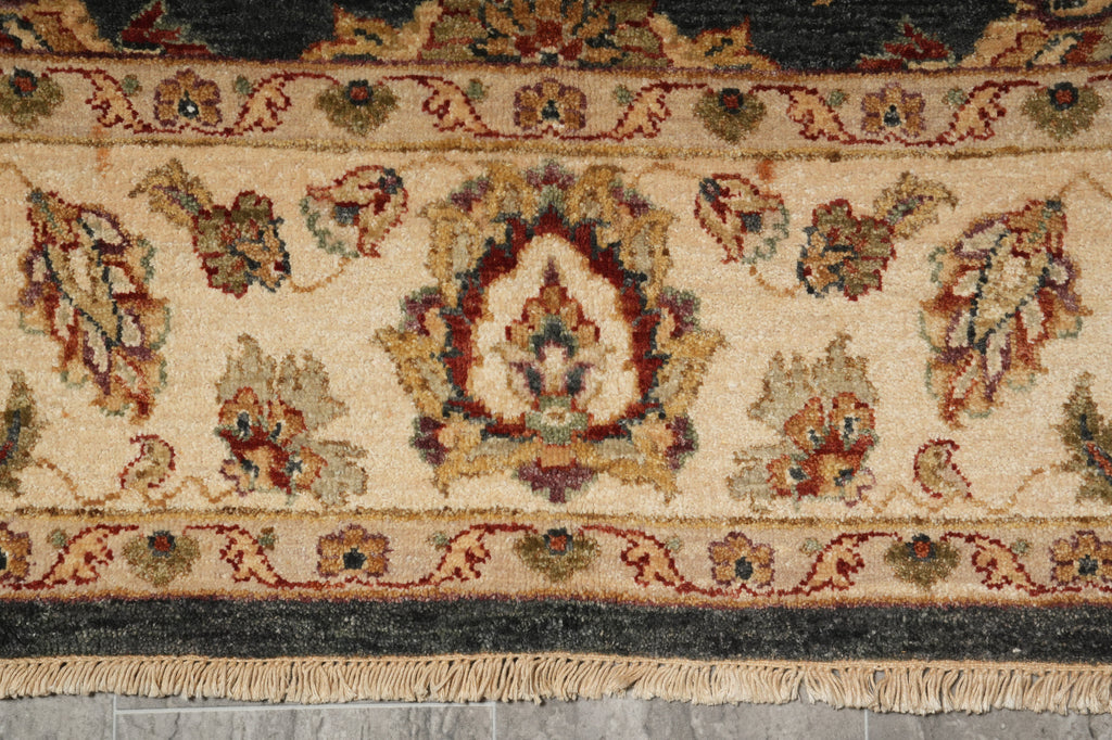 Close-up of an ornate area rug with a cream background, featuring a central medallion and floral motifs in muted red, green, and brown tones, finished with a fringed edge.
