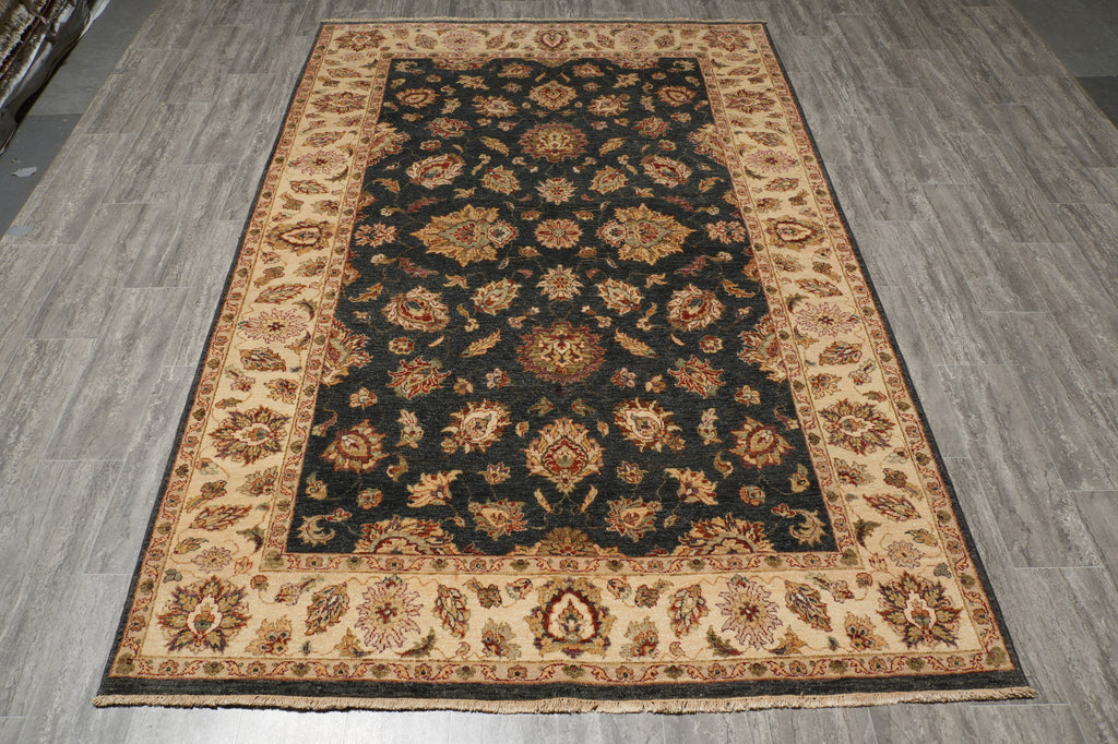 A traditional oriental area rug with a dark navy blue central field and beige borders, featuring intricate floral and medallion patterns in brown, gold, and cream, laid out on a gray wood-look floor.