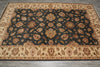 Load image into Gallery viewer, A rectangular area rug with an ornate traditional floral pattern, featuring a dark charcoal-black center field surrounded by beige borders on a gray wood floor.
