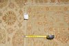 Load image into Gallery viewer, A close-up of a patterned area rug with a beige base and rust-orange floral motifs, shown with a yellow tape measure and a product tag to indicate size and details.