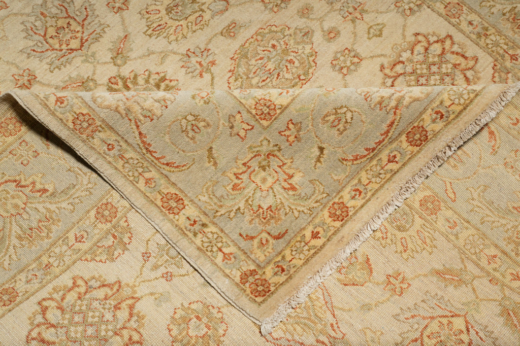 A close-up of a folded area rug with a traditional floral and medallion pattern in beige, cream, and muted rust orange tones.