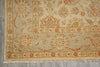 Load image into Gallery viewer, A close-up of a traditional patterned rug with a beige base and red, orange, and muted green floral motifs, showing the woven texture and fringe on a gray floor.