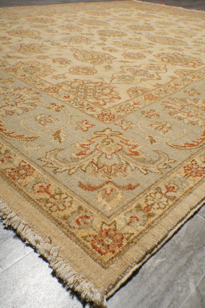 A close-up view of a traditional oriental-style area rug with a beige base, featuring a warm orange and rust floral pattern and fringed edges, laid on a gray tiled floor.
