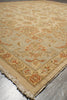 Load image into Gallery viewer, A close-up view of a traditional oriental-style area rug with a beige base, featuring a warm orange and rust floral pattern and fringed edges, laid on a gray tiled floor.