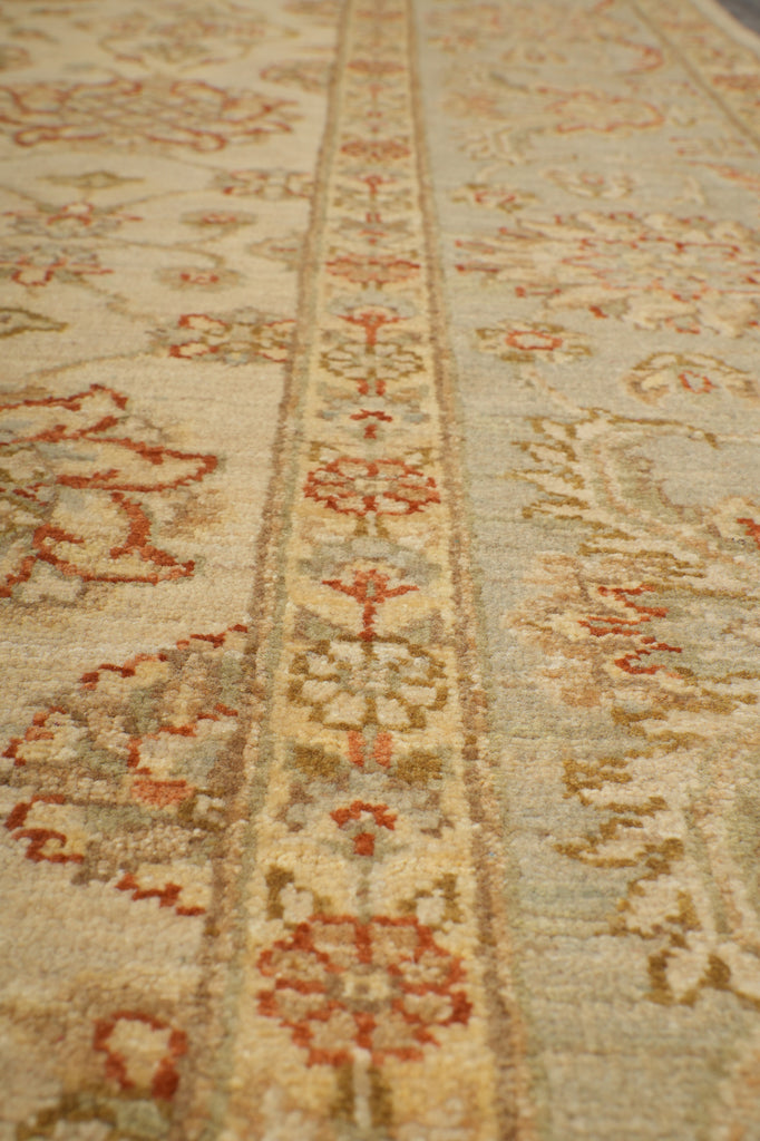 A close-up of a traditional patterned rug with a beige base and red, brown, and gray floral motifs.