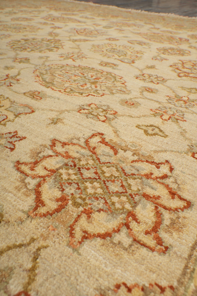 Close-up of a patterned area rug with a cream base and rust-orange floral motifs.