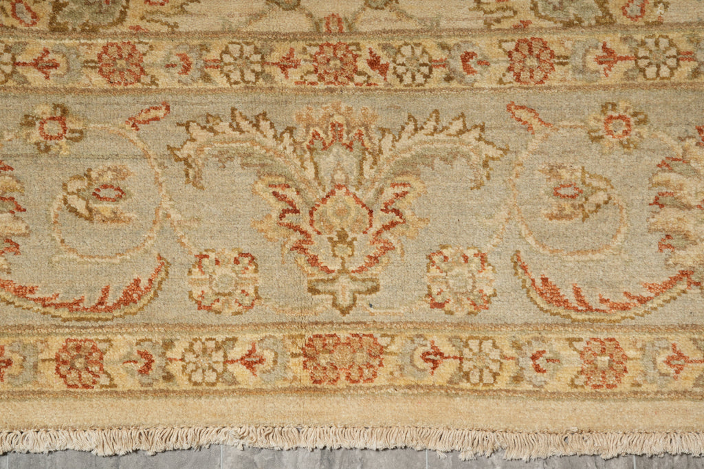 A close-up of a traditional patterned rug with a beige base, featuring red and brown floral motifs and a fringed edge.