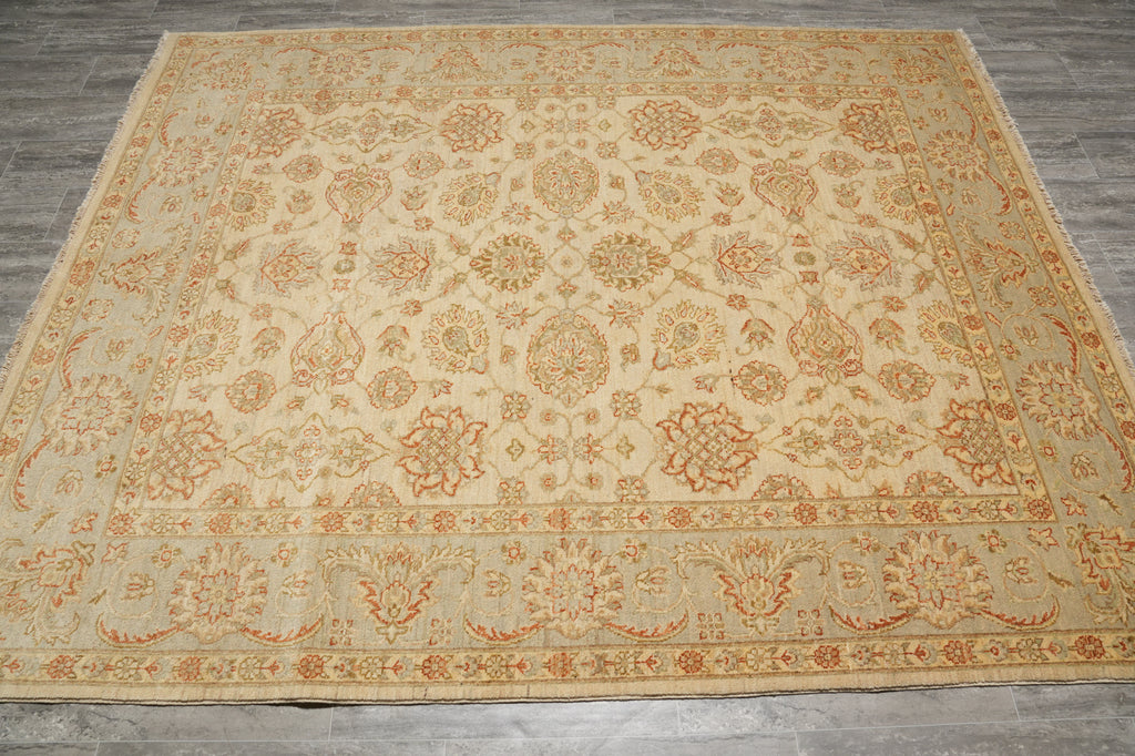 A large rectangular area rug with an intricate traditional floral and medallion pattern in beige, cream, and rust orange, laid out on a gray wood floor.