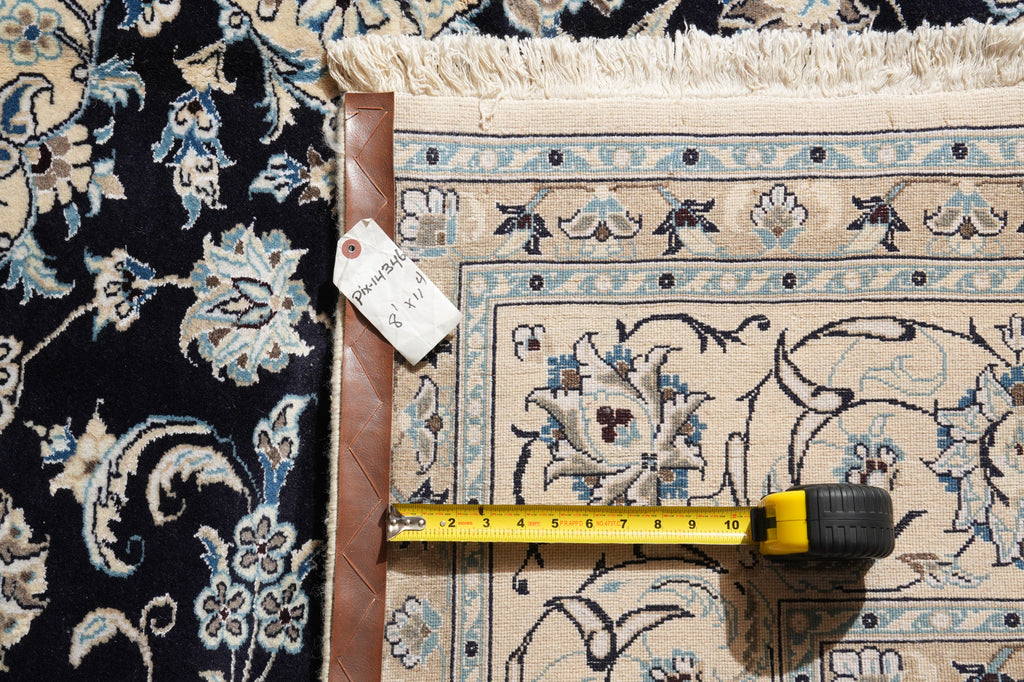 A close-up of a patterned area rug with a tape measure laid across it to show scale, next to a leather corner protector and a price tag.