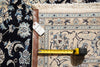 Load image into Gallery viewer, A close-up of a patterned area rug with a tape measure laid across it to show scale, next to a leather corner protector and a price tag.