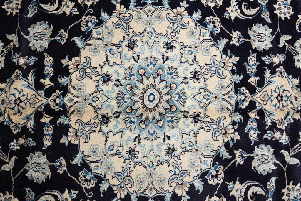 A close-up of an ornate traditional patterned rug with a central medallion and floral motifs in cream, light blue, and black.