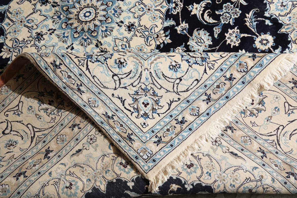 A folded traditional patterned rug with cream, navy, and light blue floral motifs and fringe trim.