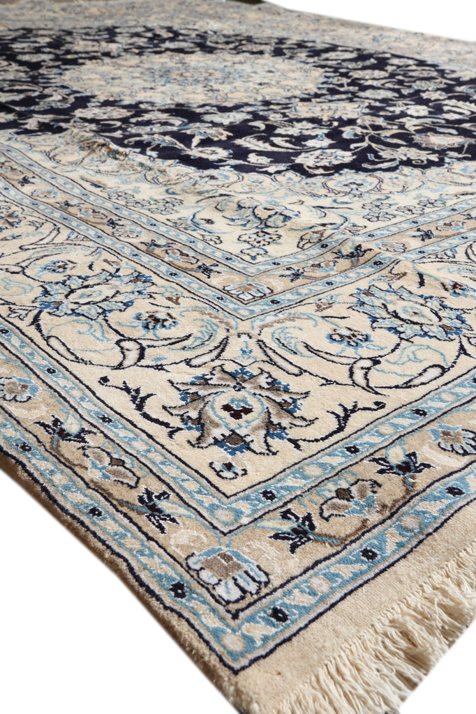 A close-up of a traditional oriental rug with a cream base, navy blue central field, and light blue and beige floral motifs.