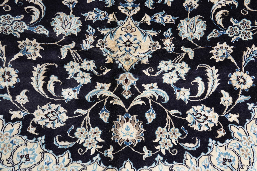 A close-up of an ornate traditional rug pattern with a dark navy blue background and cream, beige, and light blue floral and vine motifs.