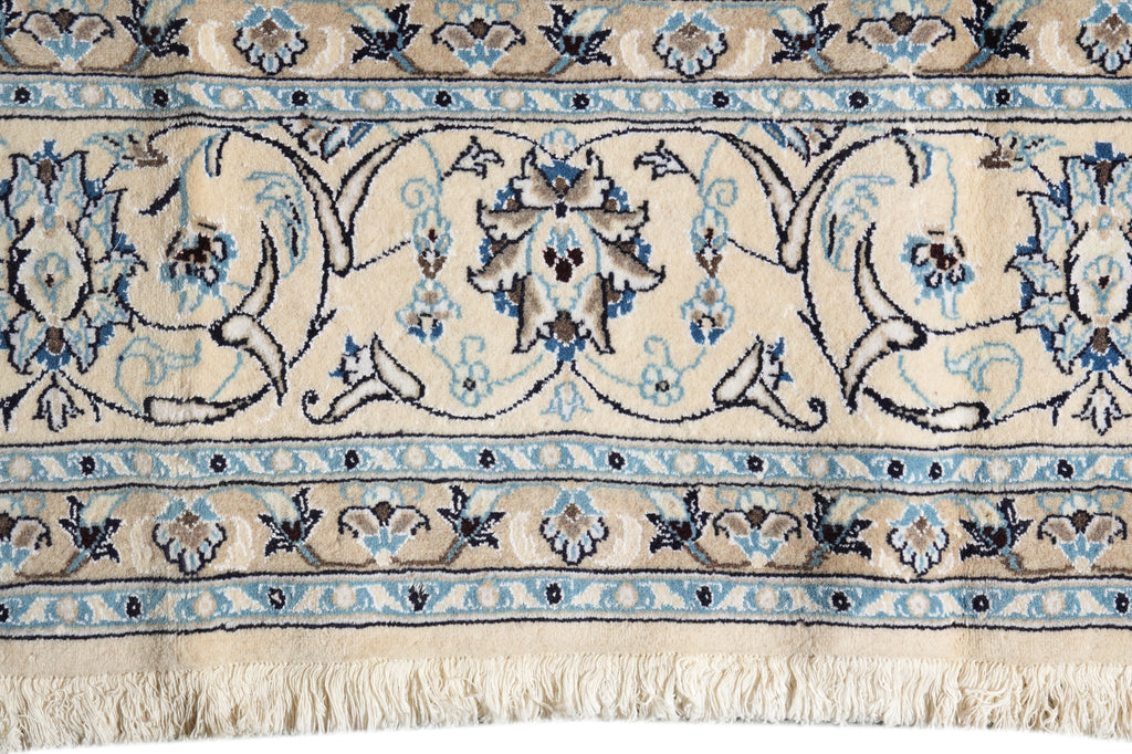 Close-up of a patterned area rug with a cream base, blue and navy floral motifs, and a fringed edge.