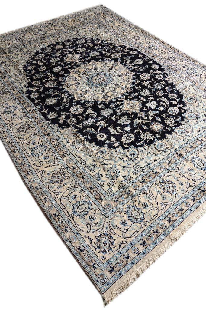 A traditional Persian-style area rug with a large central medallion, featuring a dark navy blue center surrounded by cream, beige, and light blue floral patterns and borders.