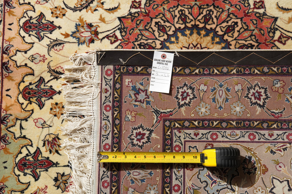 A close-up of a patterned area rug with cream fringe, shown with a tape measure and product tag to indicate size and details.