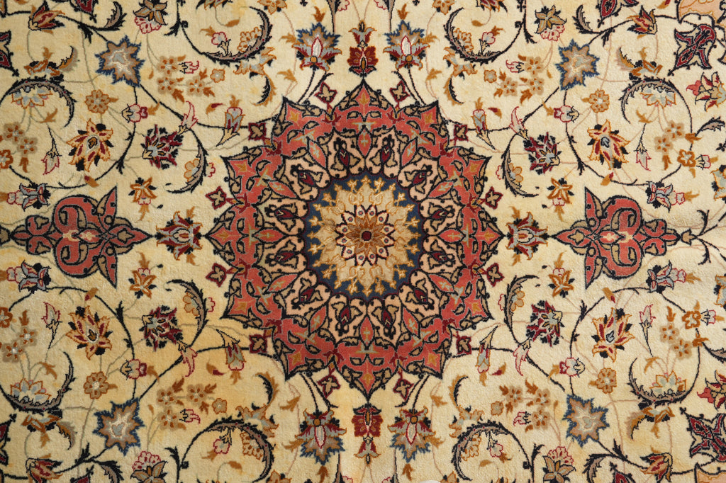 A close-up of an ornate Persian-style rug with a central floral mandala and scrolling vine motifs in beige, rust red, navy blue, and brown.