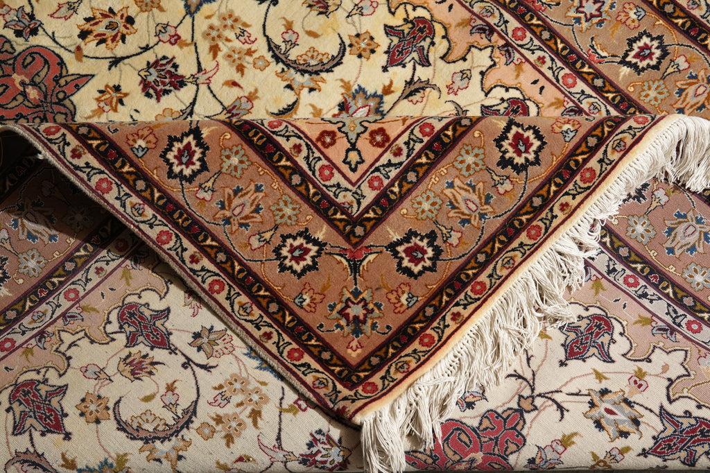 A close-up of a traditional oriental rug with a beige and brown central field, floral motifs, and cream fringe, layered over another patterned rug.