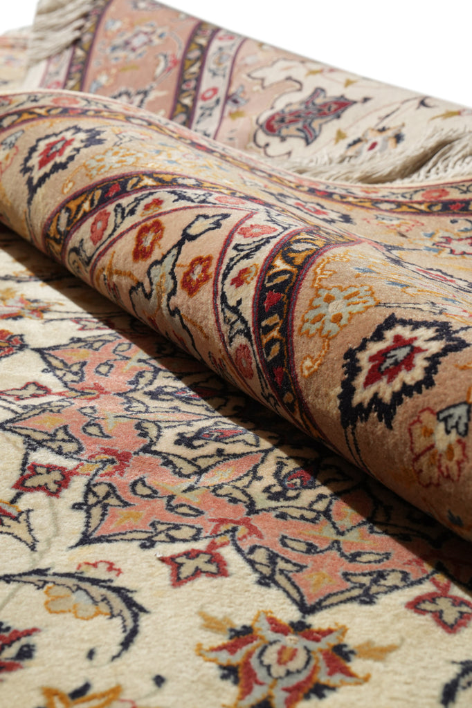 A close-up of a folded traditional patterned rug showing its detailed floral and geometric motifs in beige, cream, orange, and dark navy blue.