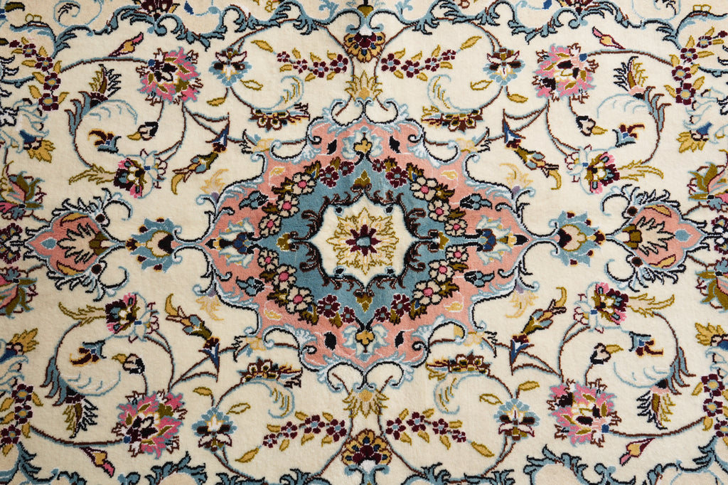 A close-up of an ornate Persian-style rug featuring a central medallion and scrolling floral motifs in soft pink, dusty blue, mustard yellow, and dark brown on a cream background.