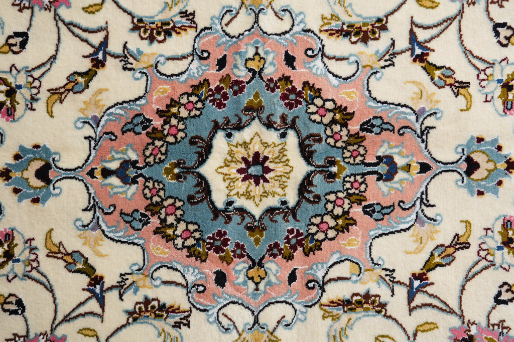 A close-up of an ornate traditional rug pattern with a central medallion in cream, dusty pink, slate blue, mustard yellow, and dark brown.