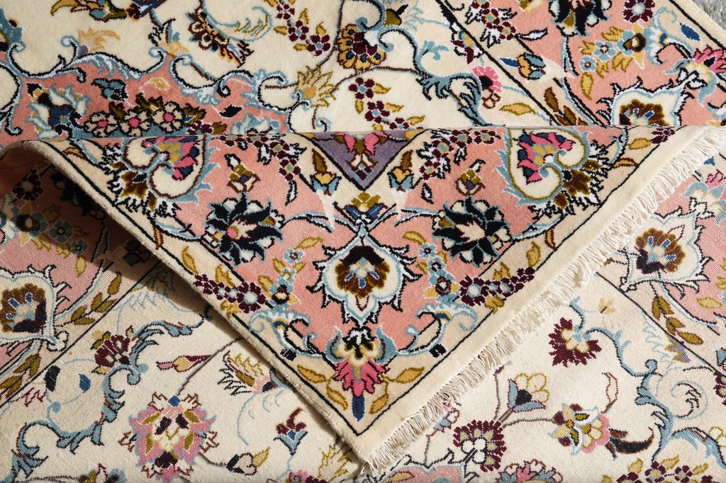 A close-up of a traditional patterned rug with cream, pink, blue, and brown floral motifs and fringed edges.