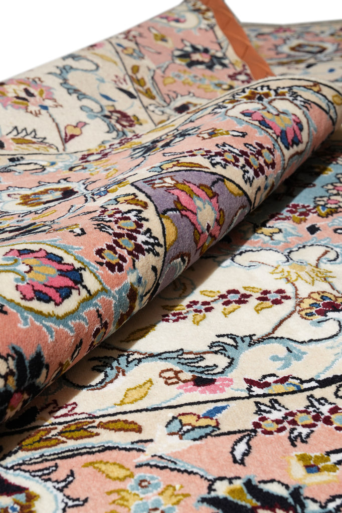 A close-up of a rolled area rug showing its detailed floral and ornamental pattern in soft pink, cream, blue, yellow, and purple tones.