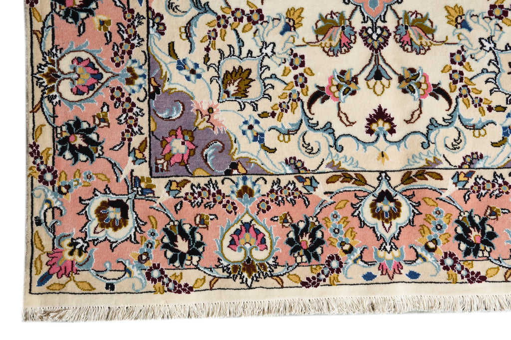 A close-up of an ornate patterned rug corner showing cream, blush pink, blue, purple, and black floral motifs with fringe along the bottom edge.