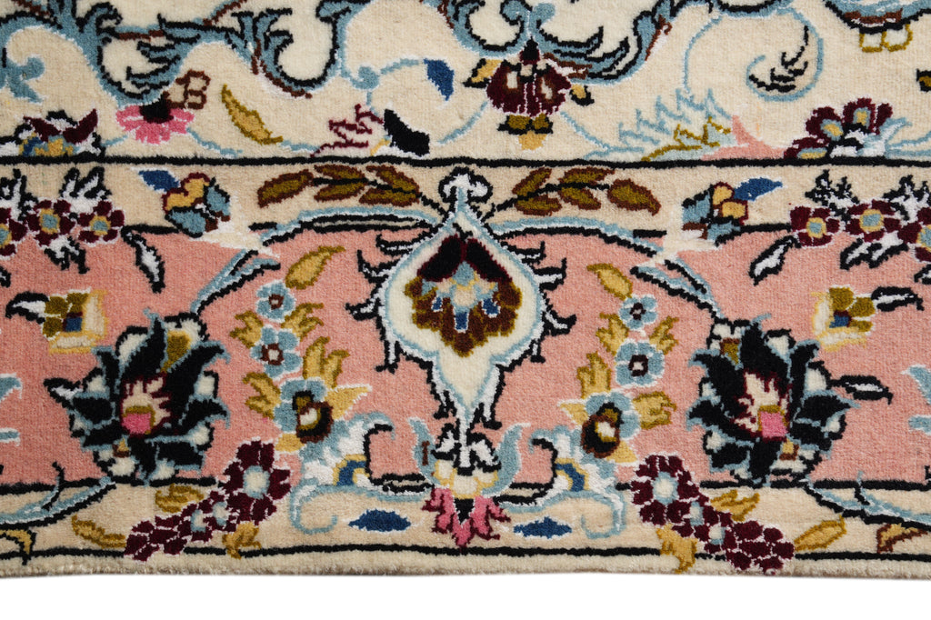 A close-up of a traditional patterned rug featuring a dusty pink field, cream borders, and a central floral medallion in blue, gold, and burgundy.